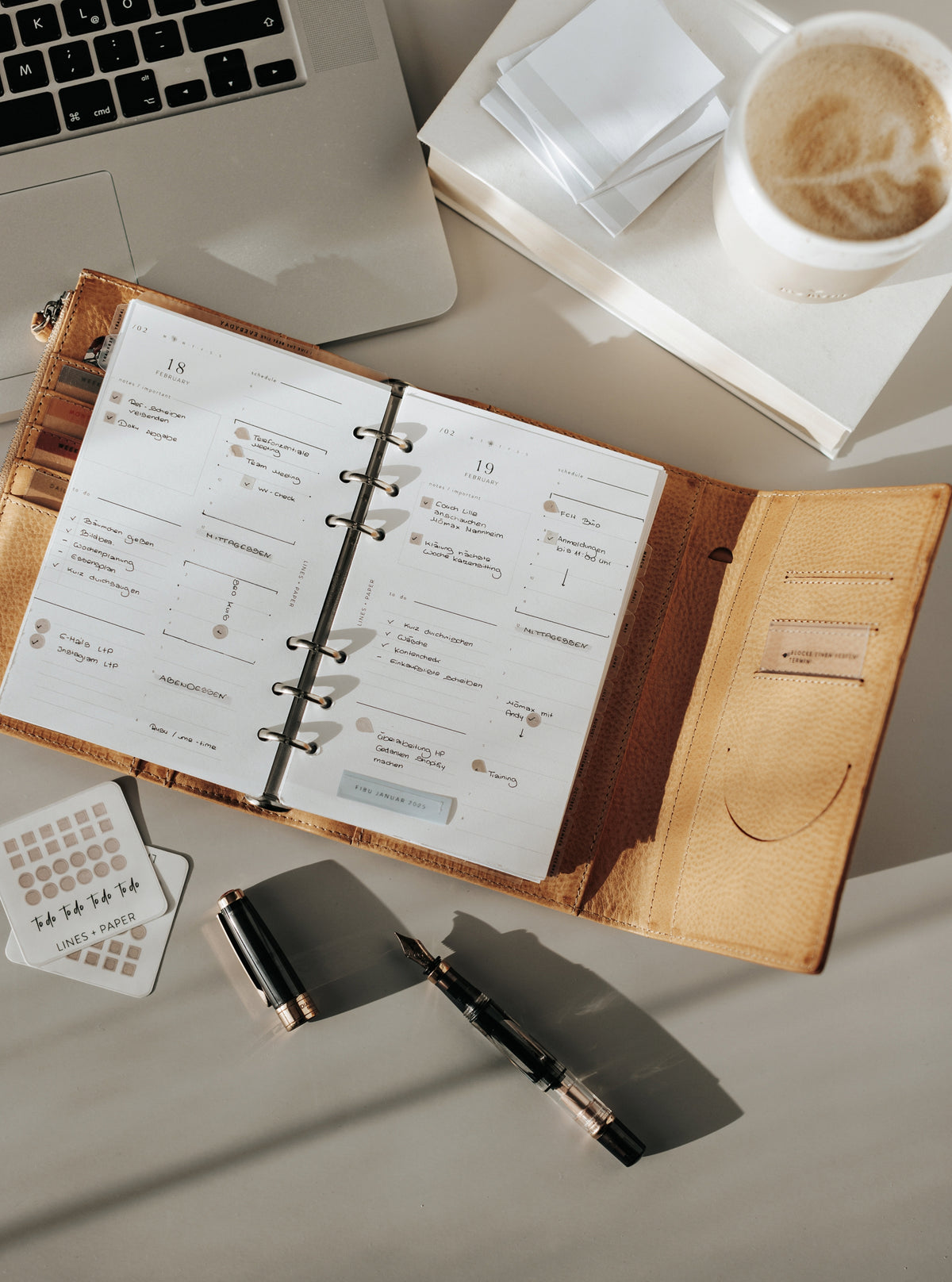 Open ring planner with printed inserts beside a laptop and coffee.